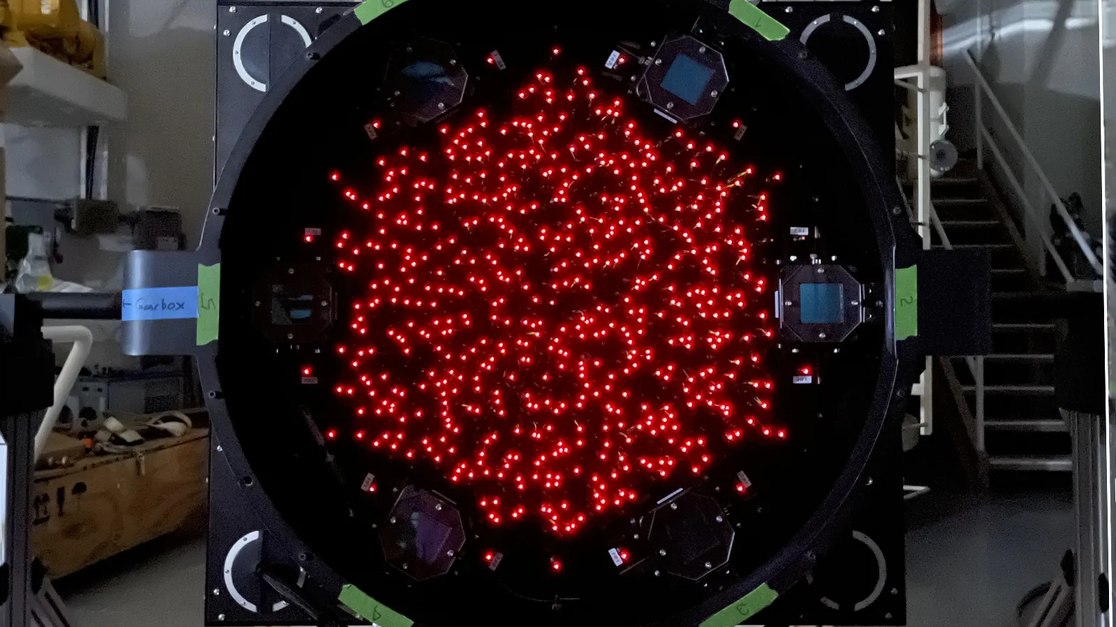 Optical fibers lit up red inside the black cylinder of an instrument inside a darkened lab