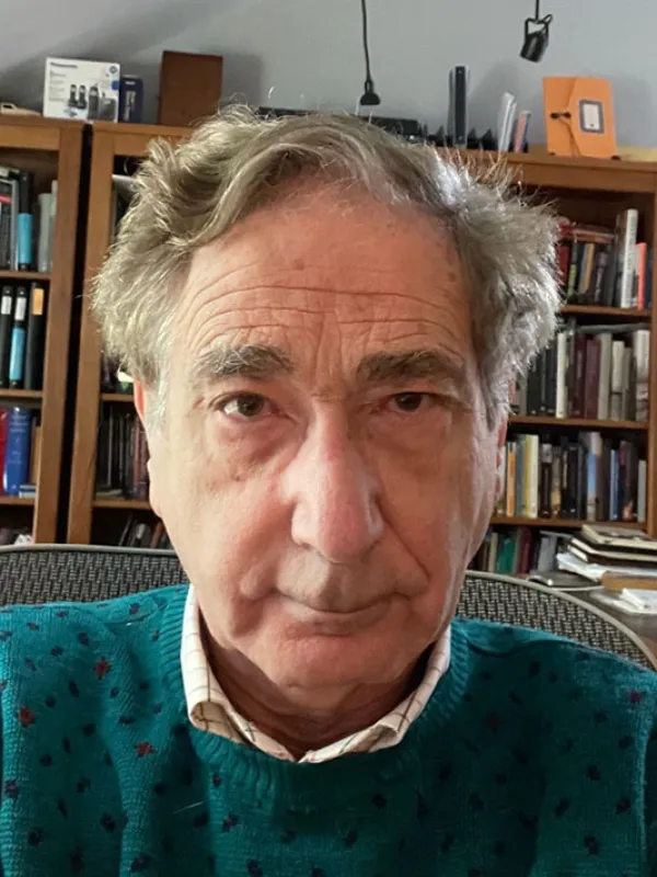 A man wearing a dark green sweater in front of a bookcase