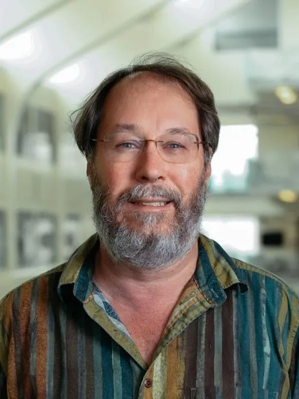 Man in a striped shirt wearing glasses with a gray beard